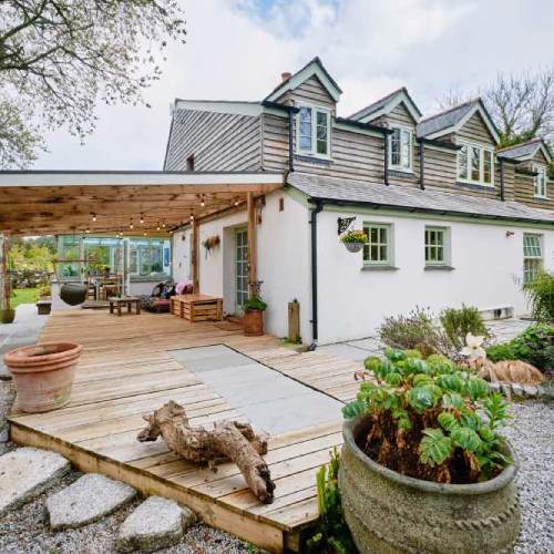 Image of the old main house at Pengelly Retreat, White cottage with wood cladded first floor. There is a covered decked area with fairy lights at a peaceful yoga retreat in Cornwall.