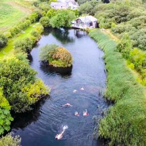 small lake with people wild-swimming, cold-water swimming. Lake is surrounded by countryside with a small island in it. Peaceful yoga retreat in Cornwall