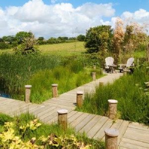 wooden jetty in an L shape looking out over a blue lake in the countryside. The sun is shining and there are 2 wooden chairs at the end to relax in and enjoy the view at the peaceful yoga retreat in Cornwall